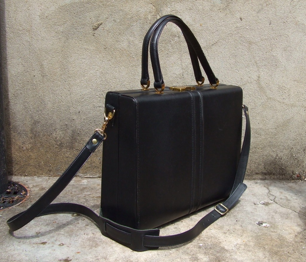 before: dark handbag with two handles and long strap against a wall