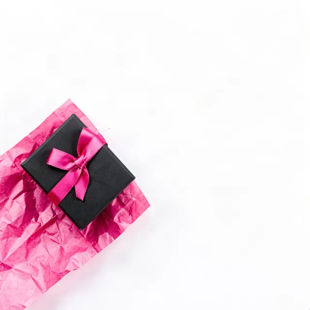 Black gift box with a hot-pink bow on pink tissue in a white corner