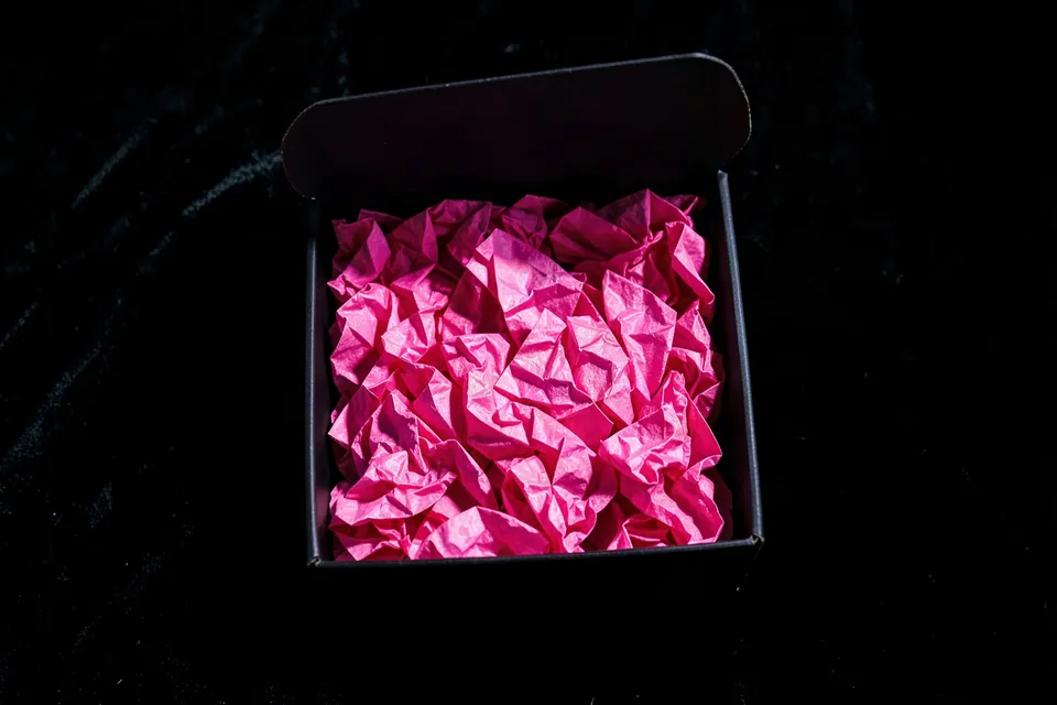 Open black gift box filled with crumpled hot-pink tissue paper