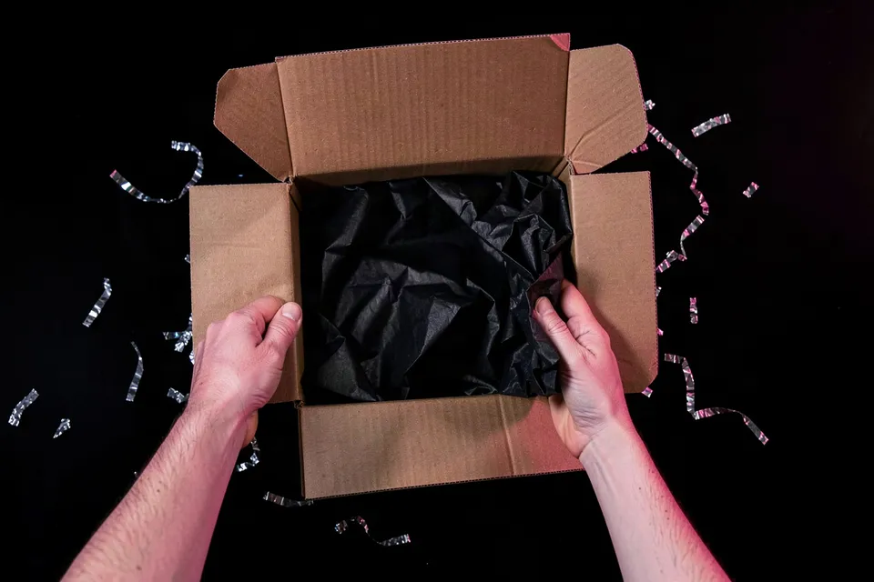 Hands opening a cardboard parcel with black tissue and silver confetti