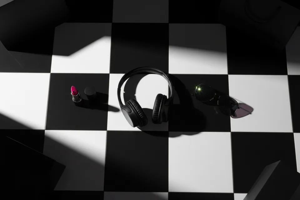 Headphones, sunglasses and a pink lipstick on a black and white checkerboard