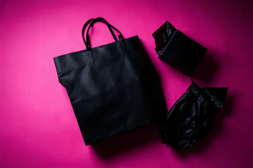 Black shopping bag and gift boxes on a hot-pink background, seen from above