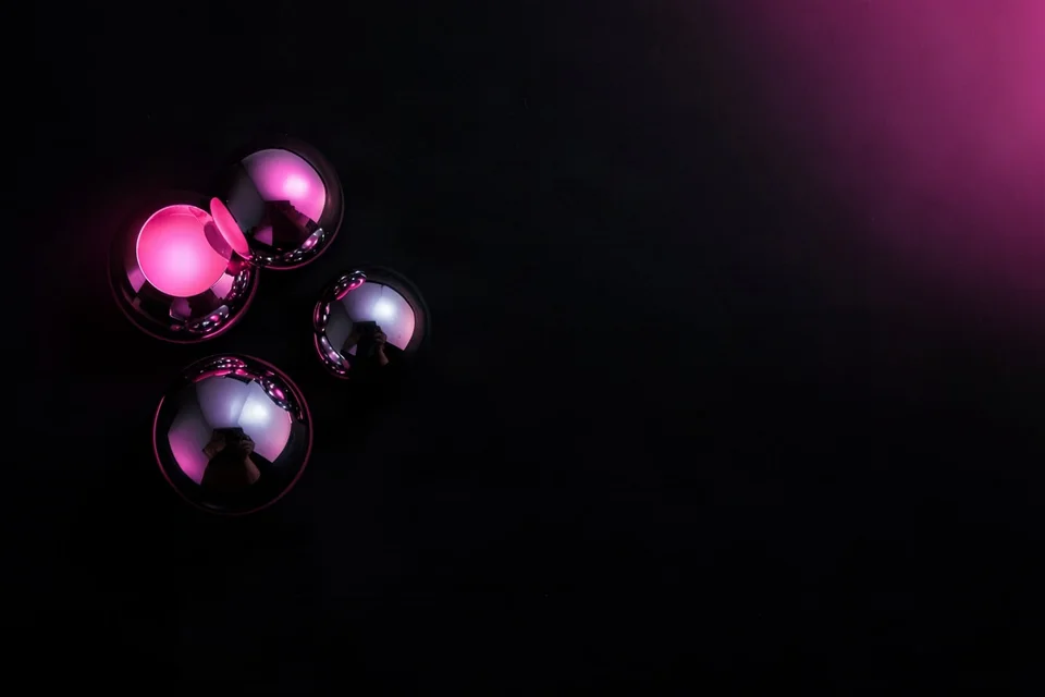 Three chrome spheres reflecting pink light on matte black paper