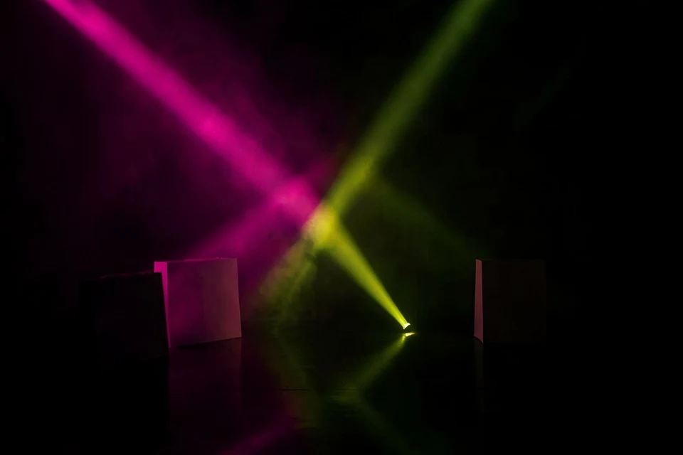 Pink and yellow-green light beams crossing in a dark foggy room