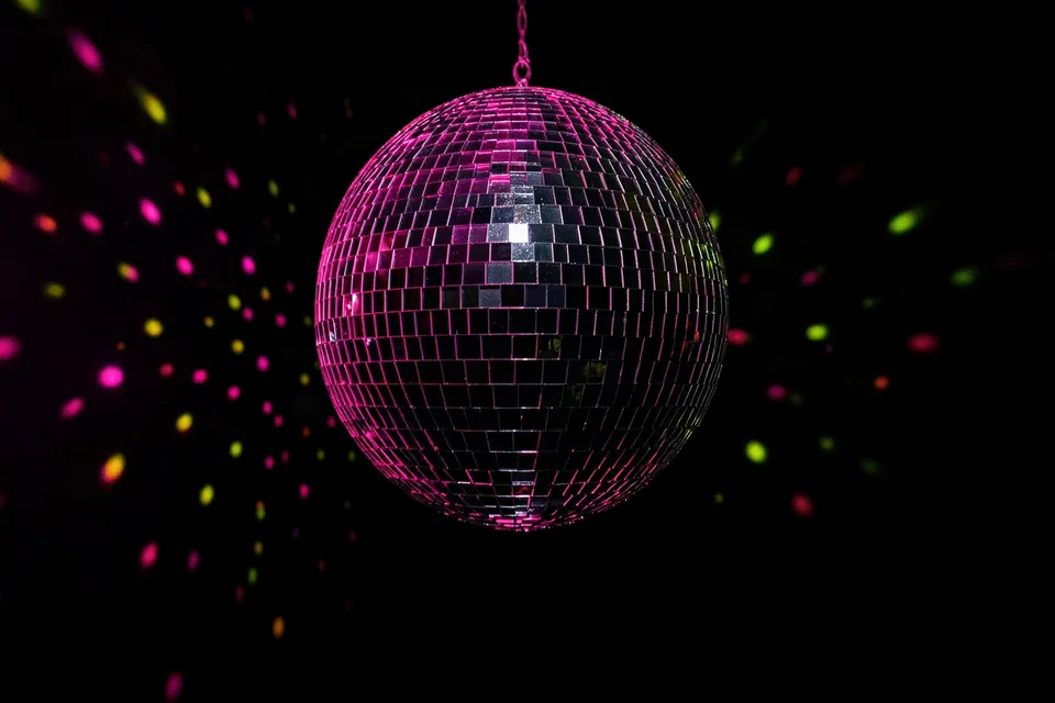 Mirrored disco ball scattering pink and green light in a dark room