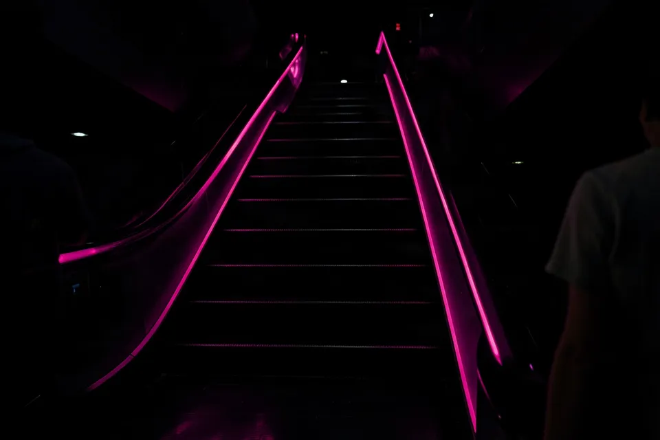 Empty mall escalator at night with glowing pink handrails, a Black Friday picture for Stories