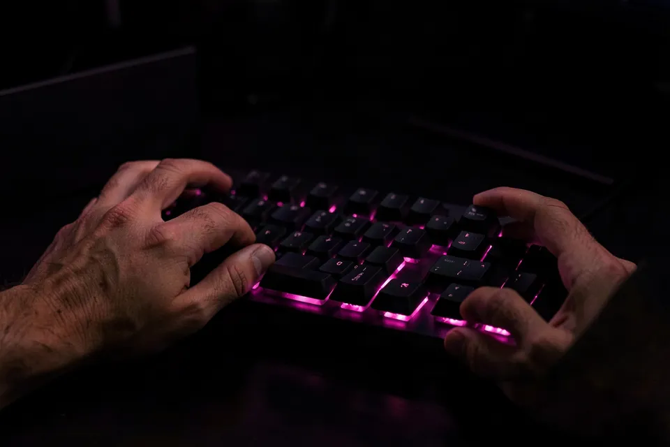 Hands typing on a black keyboard with a pink underglow, a Cyber Monday sale image