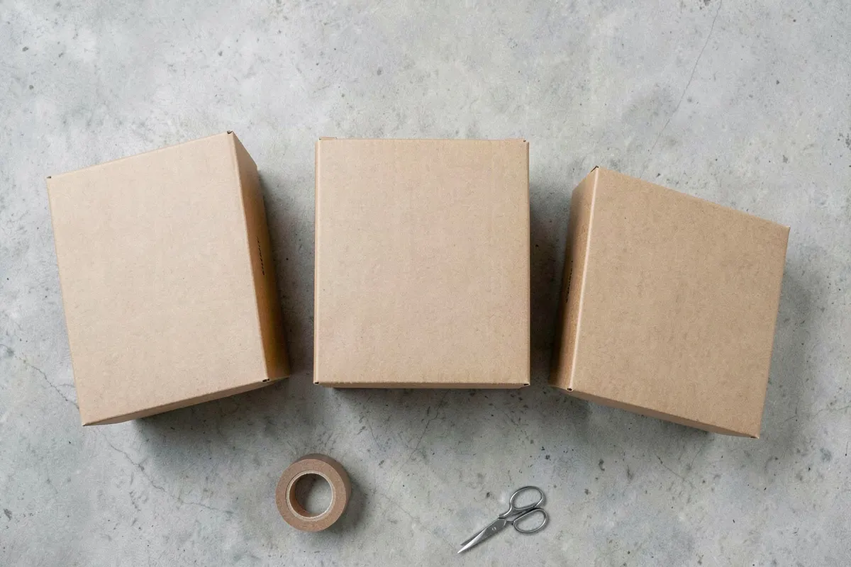 Three kraft shipping boxes on gray concrete with packing tape and small scissors