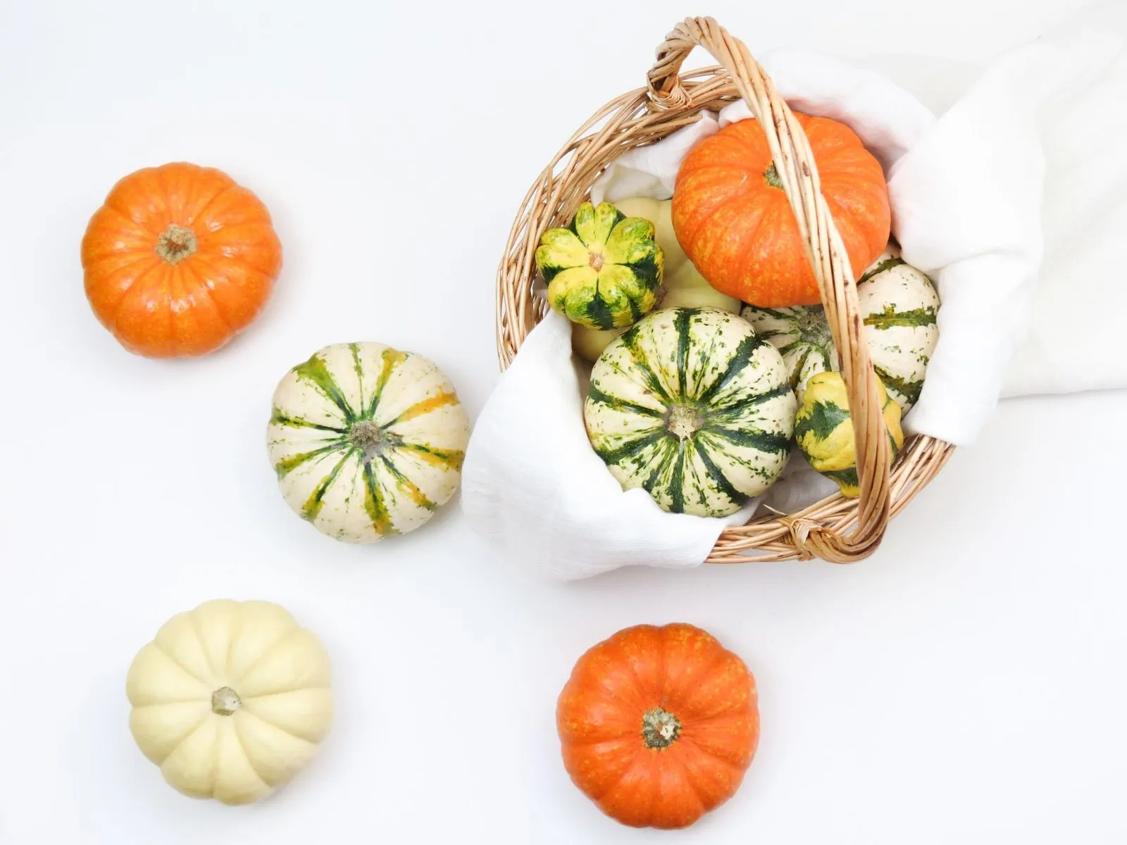 Woven Boo Basket of mini pumpkins and striped gourds on a white cloth
