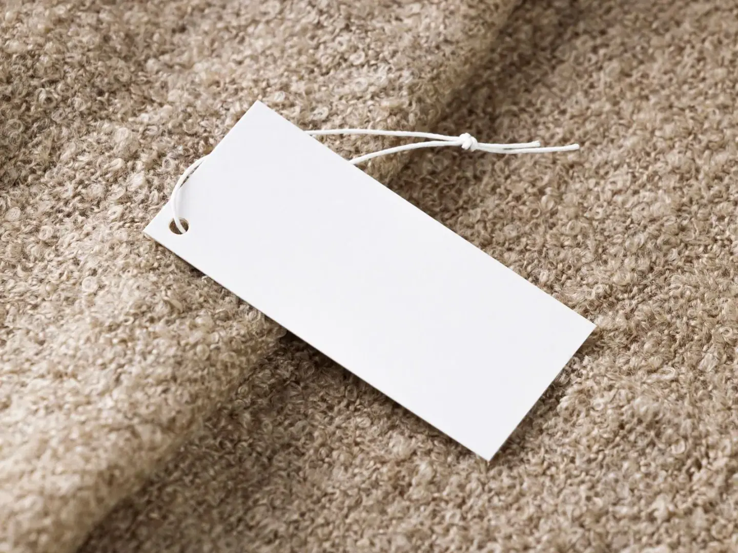 Blank white paper hang tag with string resting on a beige knit sweater