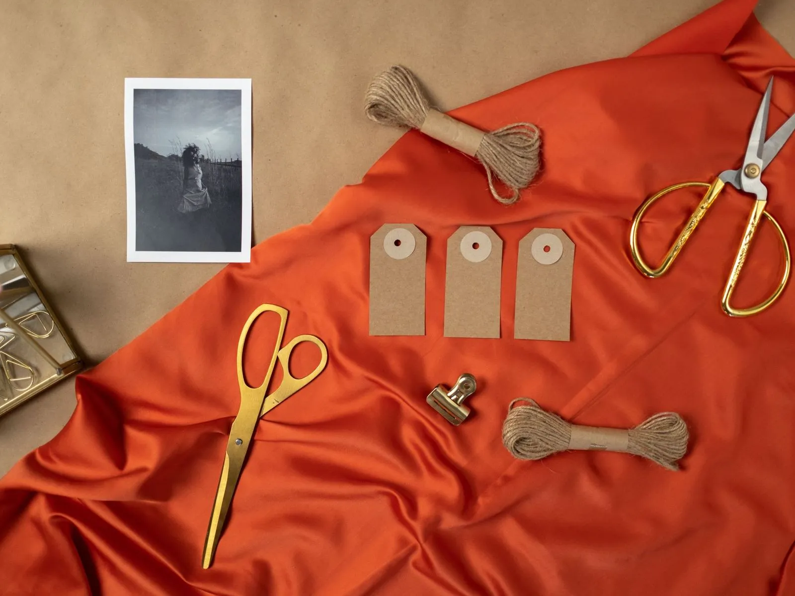 Blank kraft hang tags with twine, gold scissors and a clip on orange fabric