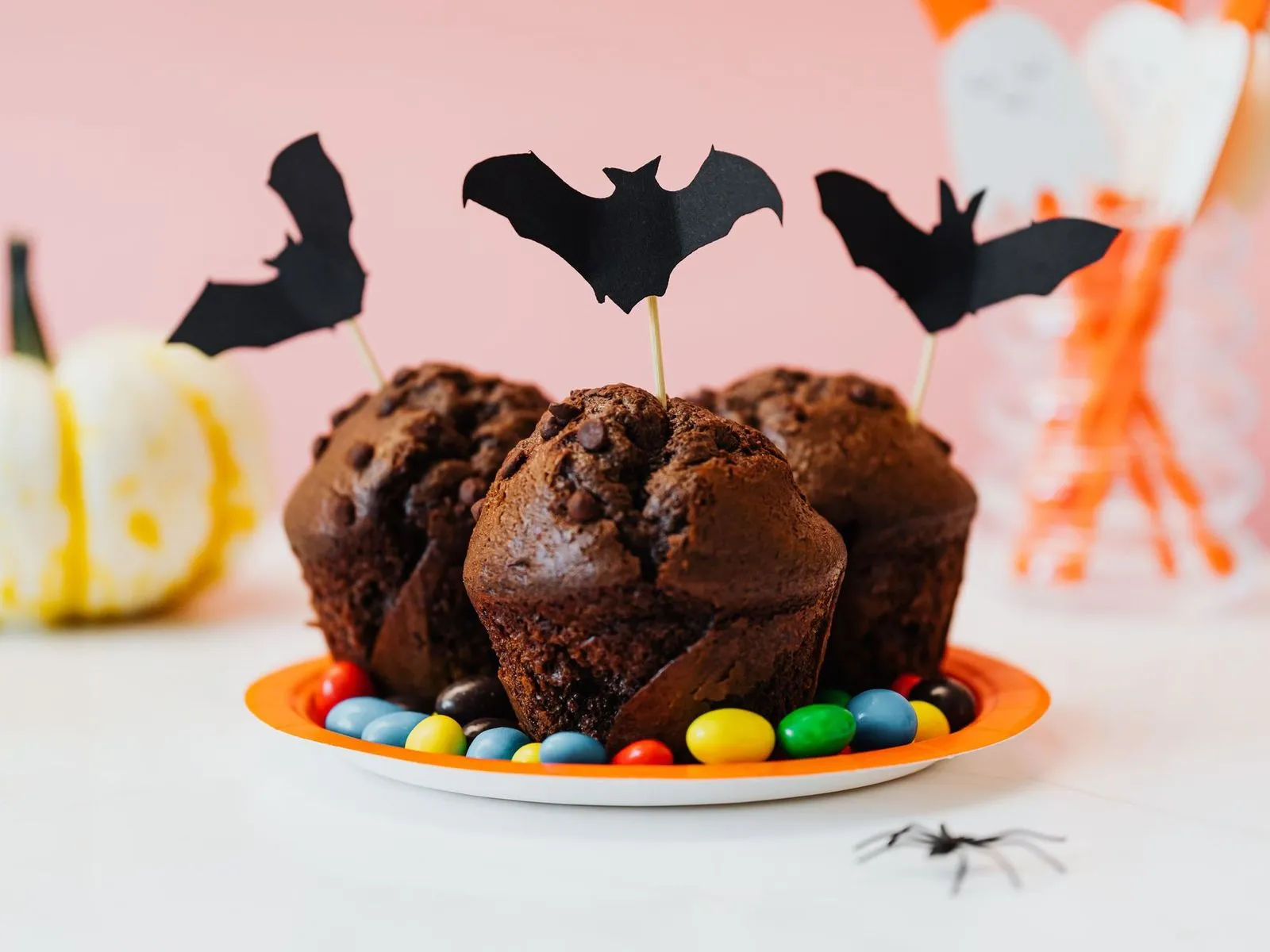 Chocolate muffins with black paper bat toppers on a pastel pink Halloween party table