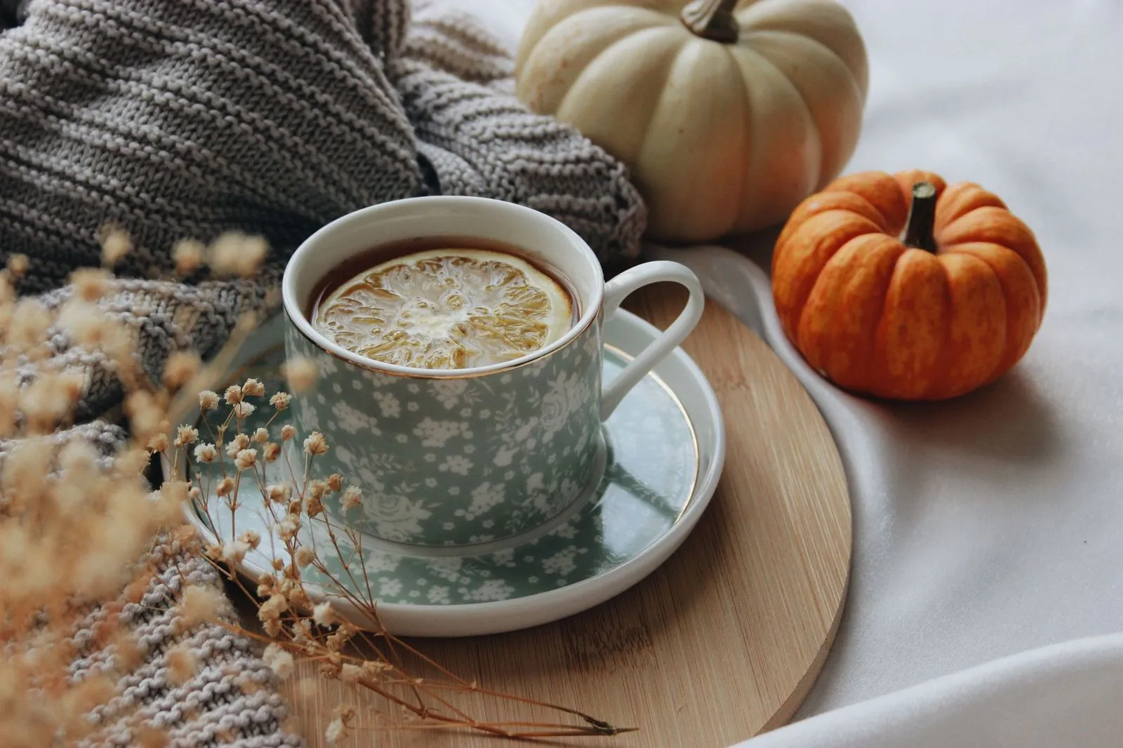Floral teacup on a wooden tray beside a knit throw with white and orange pumpkins