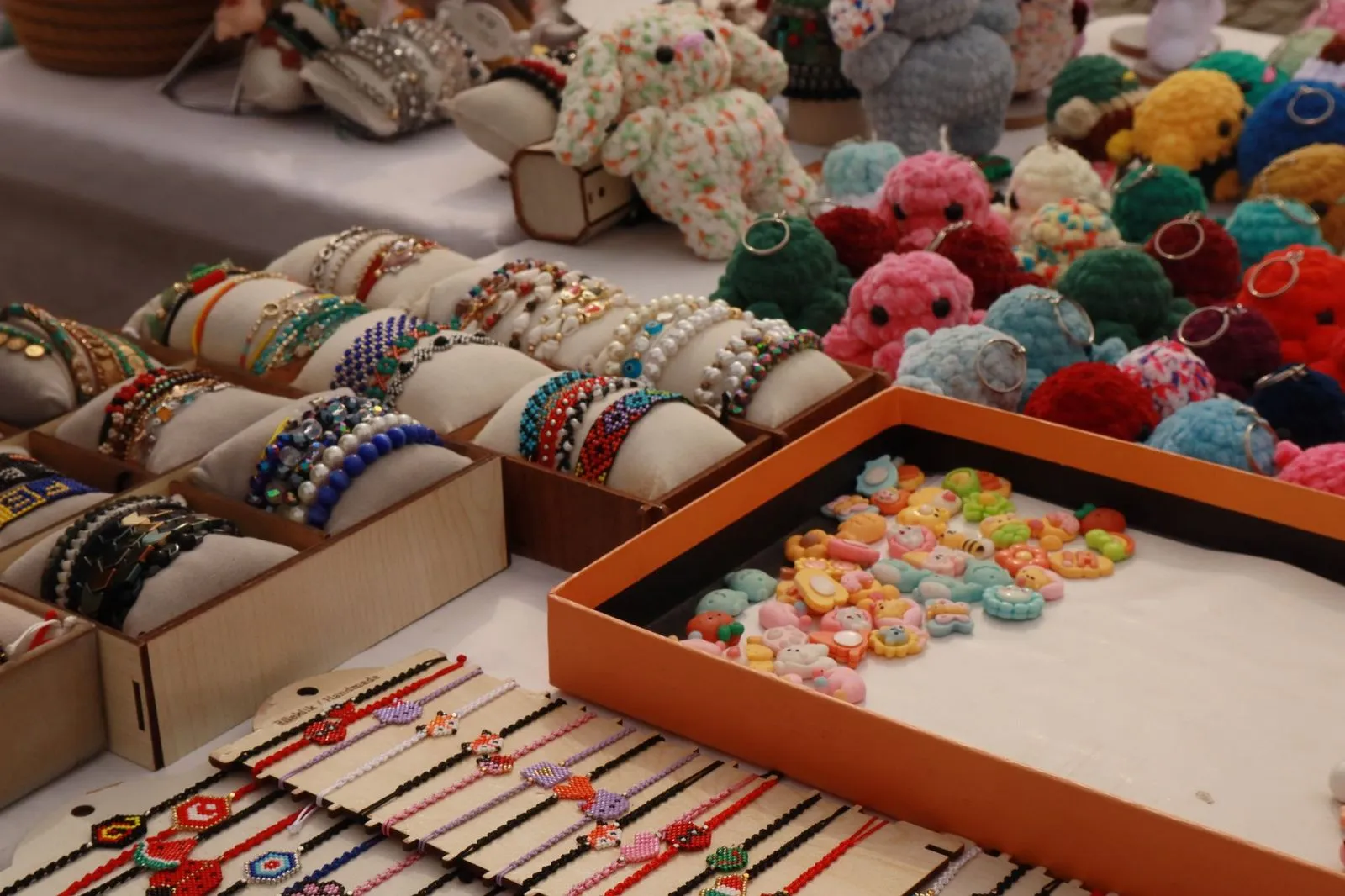 Market stall trays of handmade beaded bracelets, crocheted toys and clay charms