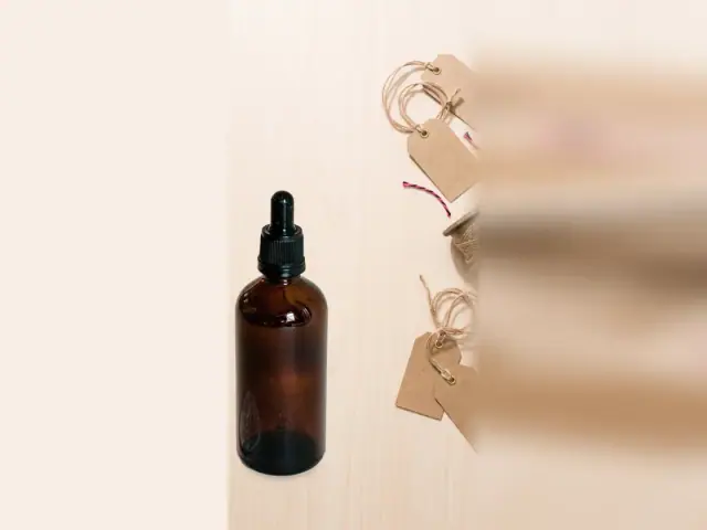 Amber dropper bottle on a light wooden table with blank kraft sale tags on twine