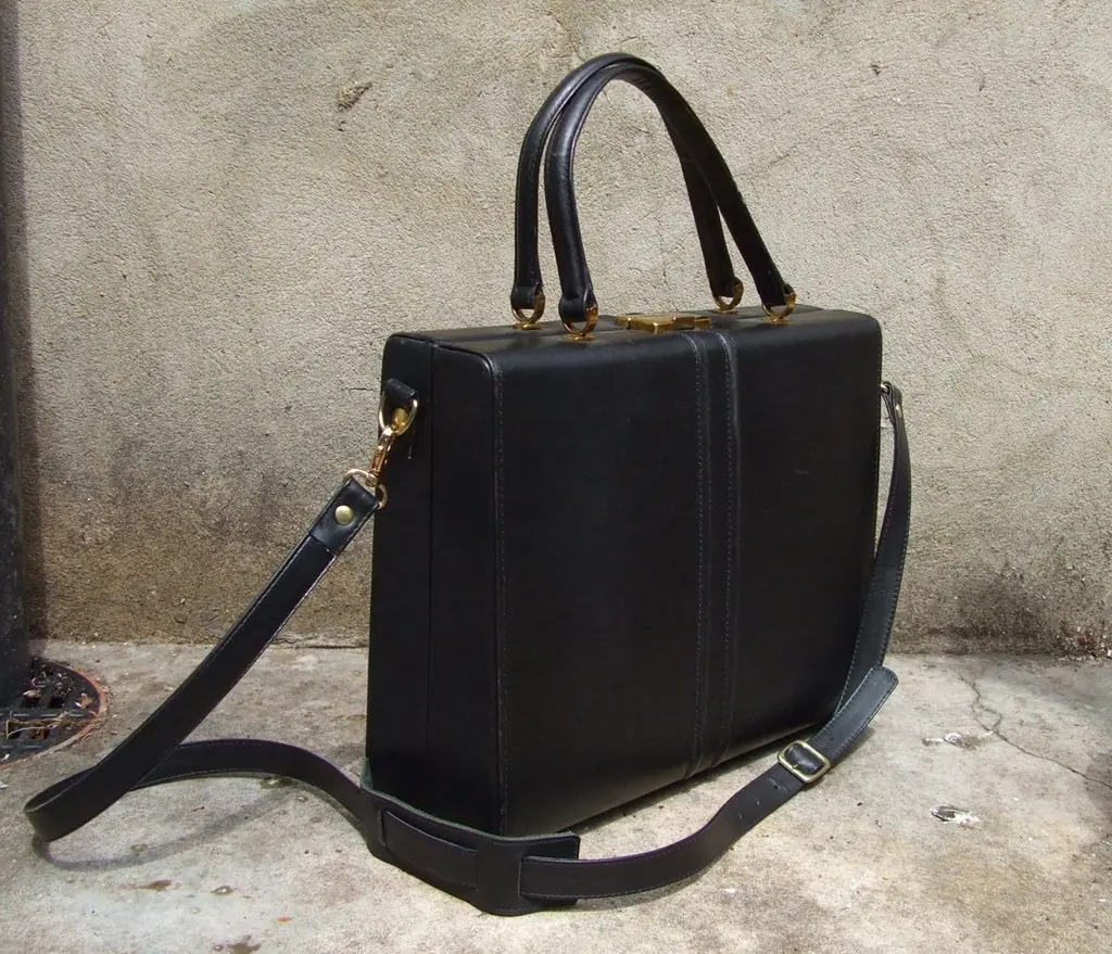 before: dark handbag with two handles and long strap against a wall