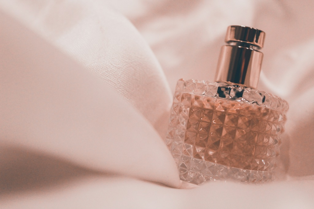 Product photo of a pink perfume bottle with a gold cap on a table